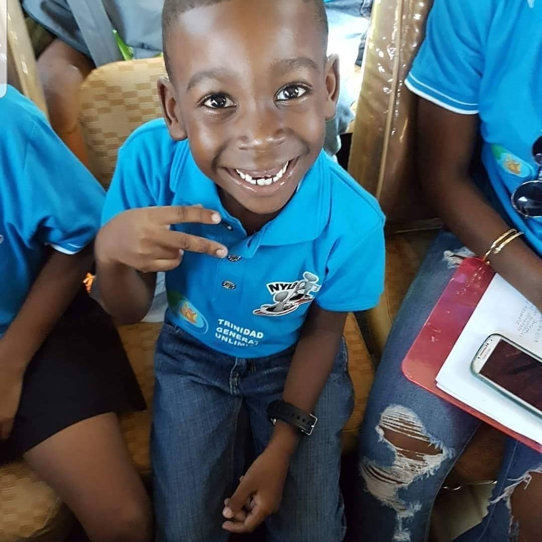 Beaming young boy in NYLB blue polo flashing a peace sign indoors.