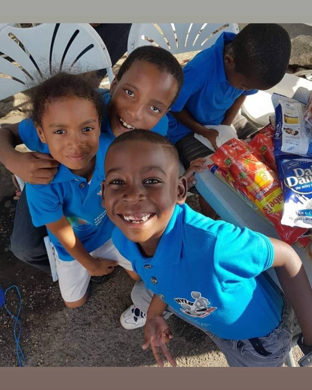 Three beaming young children in blue NYLB shirts looking up at the camera.