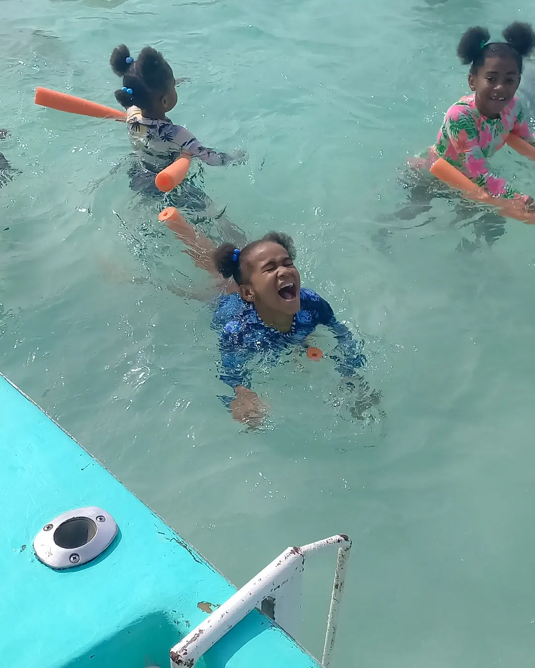 Laughing girl swimming in clear turquoise sea with a float noodle.