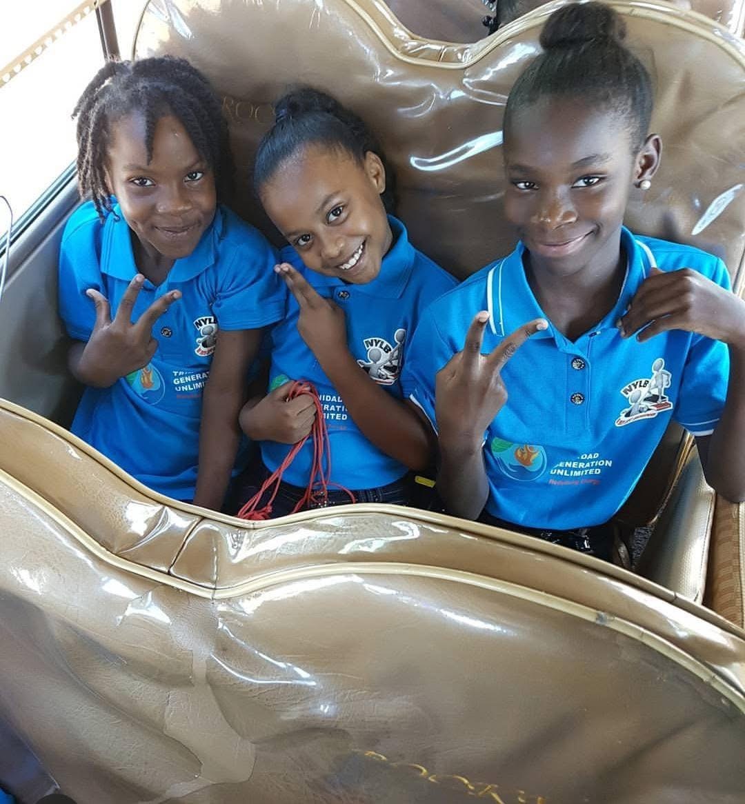 Three smiling girls in NYLB blue shirts giving peace signs.