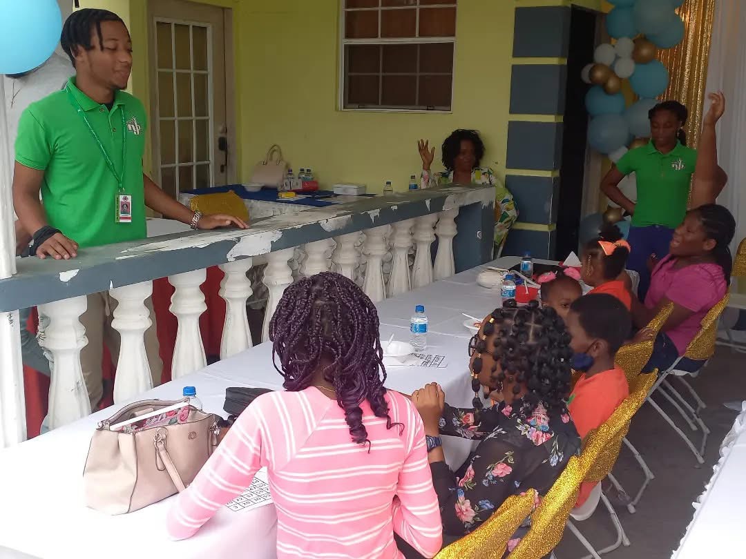 NYLB facilitator engaging children seated at a table on a community verandah.